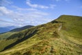 Hillsides, grassy meadow and green trees against scenic mountain backdrop beneath blue sky and white clouds Royalty Free Stock Photo