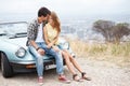 Hilltop romance. Cute young couple sitting on the hood of their convertible while on a break from their roadtrip. Royalty Free Stock Photo