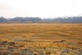 Hilly steppe dried up in autumn at the foot of high mountains covered with snow