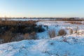Hilly terrain with dry grass covered with snow. Countryside houses on the horizon. Winter landscape in the evening with clear blue Royalty Free Stock Photo