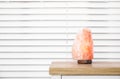 Himalayan salt lamp on wooden table near window blinds. Space for text