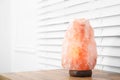 Himalayan salt lamp on wooden table near window blinds. Space for text