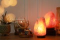 Himalayan salt lamps, candles, houseplant and gemstones on wooden table near white wall indoors. Bokeh effect