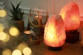 Himalayan salt lamps, candles, houseplant and gemstones on wooden table near white wall indoors. Bokeh effect