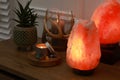 Himalayan salt lamps, candles, houseplant and gemstones on wooden table near white wall indoors