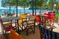 Tables and multi-colored chairs of a summer cafe on the promenade. Vacationers on beautiful clean city public beach with pine