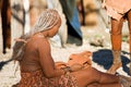 Himba woman sits on the ground.