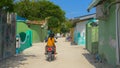 Two locals ride an old scooter down an empty road in a poor village in Maldives Royalty Free Stock Photo