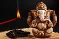 Hindu god Ganesh on a black background. Rudraksha statue and rosary on a wooden table with a red incense stick and incense smoke Royalty Free Stock Photo