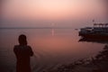 A hindu man praying during sunrise on the river Ganges in Varanasi, India. Fog, seagulls and boat silhouettes