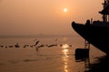 A hindu man praying during sunrise on the river Ganges in Varanasi, India. Fog, seagulls and boat silhouettes Royalty Free Stock Photo