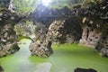 Hinged bridge over a picturesque pond in the rocks overgrown with silt