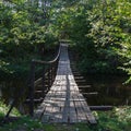 Hinged wooden bridge over a small river in the forest Royalty Free Stock Photo