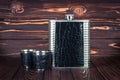 Hip flask for whiskey and two stainless steel lip tumbler on a dark brown wooden table. Bar tools. Drinkware