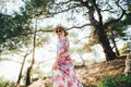 A hippie girl in a beautiful flying dress, hat and round glasses in a pine forest among the mountains.