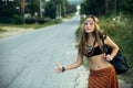 Hippie girl voting near the country road. Hitchhiking. Royalty Free Stock Photo