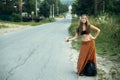 A hippie girl voting near the country road. Hitchhiking trips. Royalty Free Stock Photo