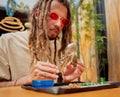 Hippie style man examines under a magnifying glass the joints and buds of medical marijuana