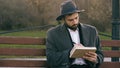 Hipser creative artist man in hat and coat drawing with pen and sketchbook sitting on city street bench at park Royalty Free Stock Photo