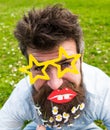 Hipster with beard on cheerful face, posing with star shaped glasses and lips. Guy looks nicely with daisy flowers in Royalty Free Stock Photo