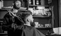 Hipster bearded client getting hairstyle. Barber on cheerful face with hairdryer styling hair of client. Barber with