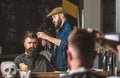 Hipster bearded client getting hairstyle. Barber with hairdryer works on hairstyle for bearded man, barbershop