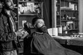 Hipster bearded client got hairstyle. Barber with hairdryer blows off hair out of cape. Barbershop concept. Barber with Royalty Free Stock Photo