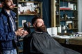 Hipster bearded client got hairstyle. Barber with hairdryer blows off hair out of cape. Barbershop concept. Barber with Royalty Free Stock Photo