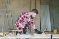 Hipster bearded man is carpenter, builder, designer stands in workshop, using laptop. On desk is construction tools