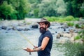 Hipster bearded man catching trout fish. Young man fishing. Fisherman with rod, spinning reel on river bank. Man