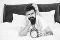 Hipster bearded man lay in bed with alarm clock. Time to wake up. Why you should wake up early every morning. Health Royalty Free Stock Photo