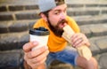 Hipster bite hot dog hold drink paper cup. Man bearded shows paper cup drink stairs background. Energy from street food