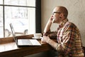 Smiling bearded businessman wearing casual hipster clothing using laptop and cell smartphone in coffe house. Royalty Free Stock Photo