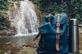 Hipster Blue Backpack, Map And Thermos Closeup. View From Front Tourist Traveler Bag On Waterfall Background. Adventure Hiking Con