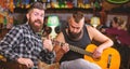 Hipster brutal bearded with friend in pub. Man play guitar in pub. Cheerful friends sing song guitar music. Relaxation