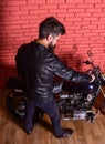 Hipster, brutal biker in leather jacket sits down on motorcycle, rear view. Man with beard, biker in leather jacket near Royalty Free Stock Photo