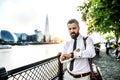 Hipster businessman with laptop bag walking by the river in London, checking the time.