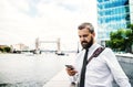 Hipster businessman with smartphone standing by the river in London, texting.