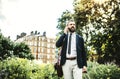 Hipster businessman with smartphone and suitcase walking in park in London. Royalty Free Stock Photo