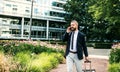 Hipster businessman with smartphone and suitcase walking in park in London. Royalty Free Stock Photo