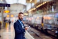 Hipster businessman with smartphone, waiting, train platform