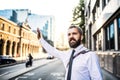 Hipster businessman standing in London, raising his shand to hail a taxi cab. Royalty Free Stock Photo