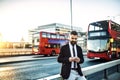 Hipster businessman standing by the road in London, using smartphone.