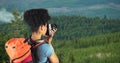 Hipster carrying backpack and photographing with camera while standing on cliff Royalty Free Stock Photo