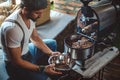 Hipster catching roasted coffee from the roaster with a dish