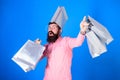 Hipster on cheerful face with bag on head is addicted shopaholic. Man with beard and mustache carries shopping bags