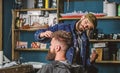 Hipster client with fresh haircut or hairstyle. Barber styling hair of bearded client with wax by hands. Barbershop
