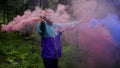 Hipster with colored smoke bombs in forest. Stock footage. Young man dispels colored smoke bombs in green forest for