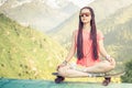 Hipster fashion girl doing yoga, relaxing on skateboard at mountain