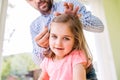 Hipster father with his daughter, styling her hair, indoors